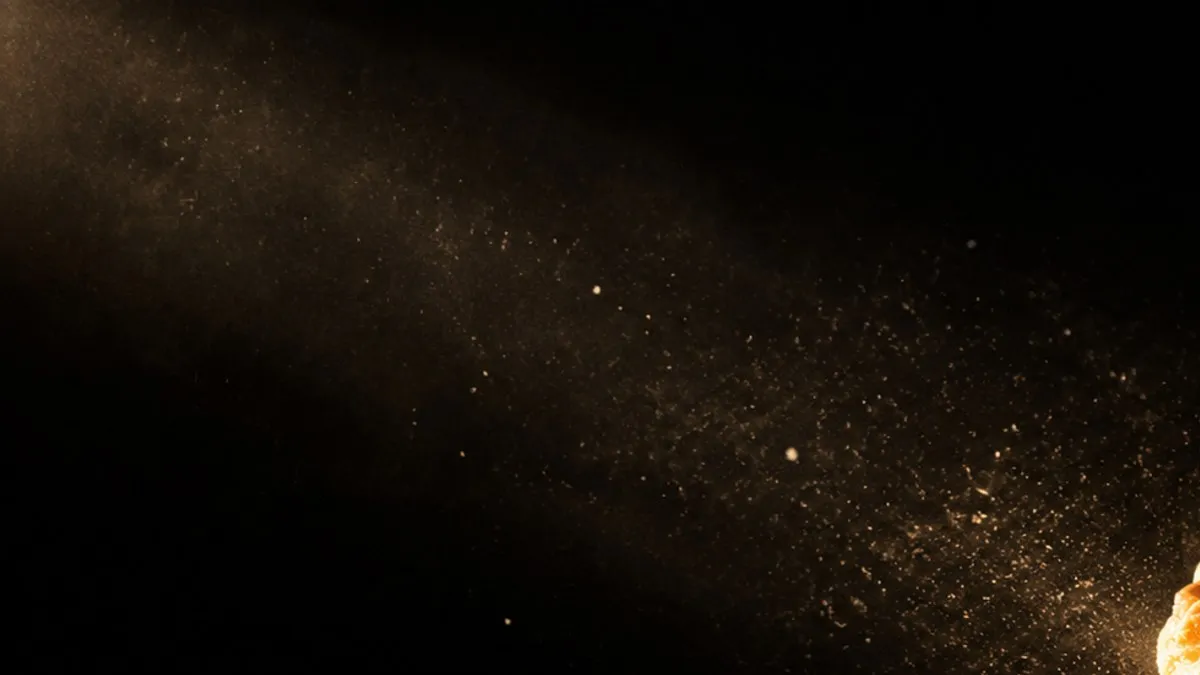 Flour dust drifting through a beam of warm light against a dark background